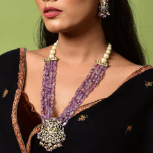 Load image into Gallery viewer, Woman wearing a black saree with gold details and a purple necklace against a green background


